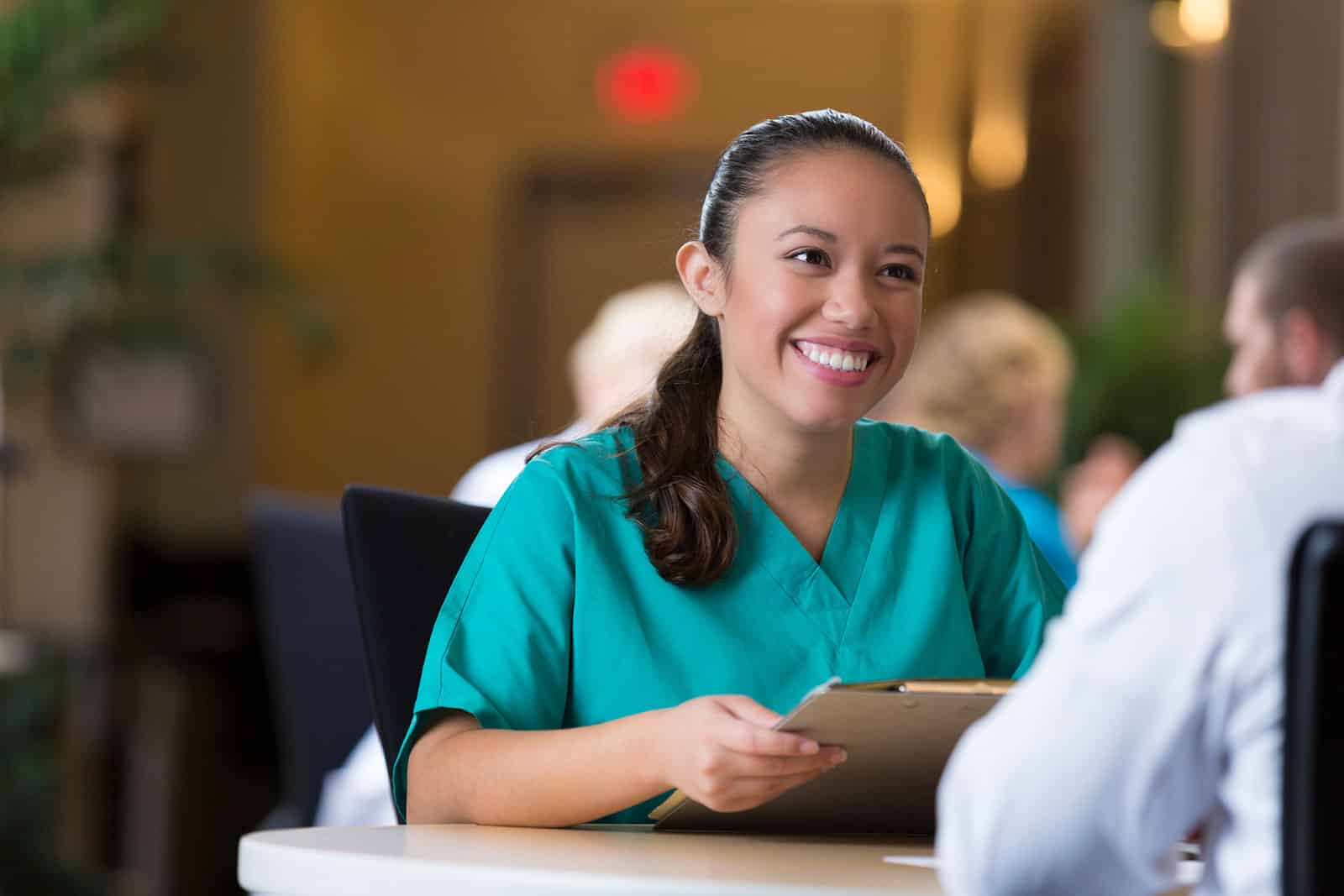 Nurse smiling and holding a clipboard while talking to an employer.